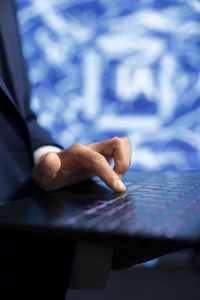 A close-up of a person's hand resting on a laptop keyboard, with a blurred blue digital background.
